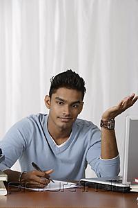 PictureIndia - young man writing at his desk, puzzled
