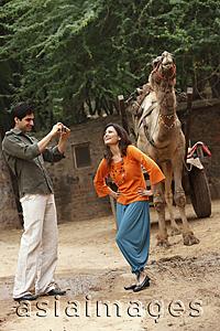 Asia Images Group - man taking photo of woman in front of camel