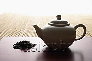AsiaPix - tea leaves in a pile and teapot on bamboo mat closeup