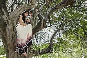 Asia Images Group - Young woman sitting in tree