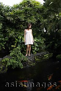 Asia Images Group - Young woman standing above koi pond