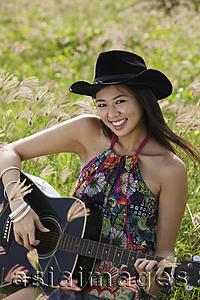 Asia Images Group - Smiling woman playing guitar in grassy field.