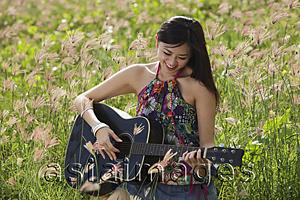 Asia Images Group - Woman playing guitar outside in grassy field.
