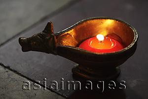 Asia Images Group - Lit candle in bronze cow dish