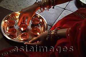 Asia Images Group - Close up of woman wearing a sari, putting oil lamps on silver tray