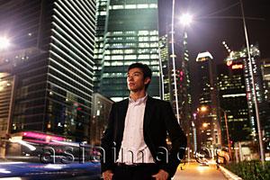 Asia Images Group - Young man standing on street at night with buildings in background