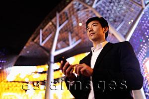 Asia Images Group - Young man in suit using phone in front of building at night
