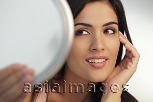 Asia Images Group - Head shot of young woman holding mirror and touching her face