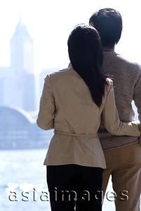 Asia Images Group - Couple standing by waterfront looking at Hong Kong skyline, rear view