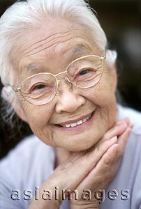 Asia Images Group - Mature woman with glasses resting chin on hands, smiling, portrait