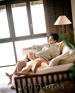 Asia Images Group - Man sitting on sofa, woman lying down with head on lap