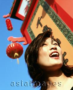 Asia Images Group - Woman laughing next to chinese sign, lantern and blue sky in background.