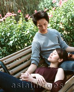 Asia Images Group - Young woman lying on bench with head on man's lap, nature in background.