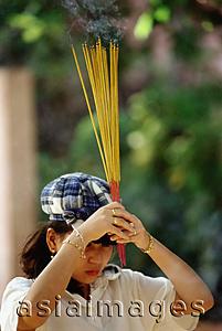 Asia Images Group - Vietnam, Ho Chi Minh City, A woman waving incense sticks during prayer.