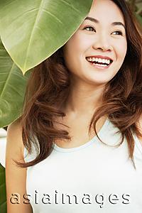 Asia Images Group - Young woman standing under leaves, smiling