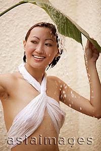 Asia Images Group - Young woman holding leaf, water cascading on her, looking away