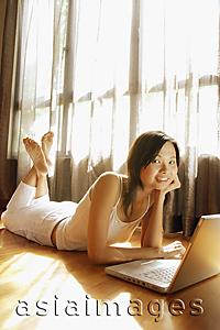 Asia Images Group - Young woman lying on floor with laptop, looking at camera