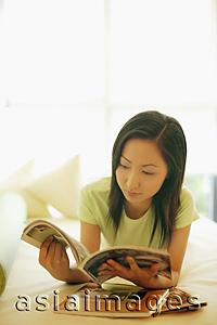 Asia Images Group - Young woman lying on bed, reading magazine
