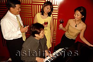 Asia Images Group - Man playing the piano, people standing around him
