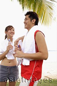 Asia Images Group - Couple standing at beach, side by side, holding water bottles