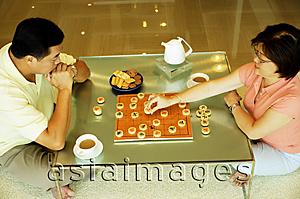 Asia Images Group - Couple sitting on floor, playing Chinese chess at home, high angle view