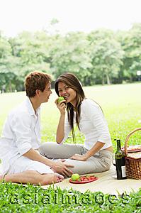 Asia Images Group - Couple having picnic in park, woman eating apple