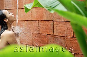 Asia Images Group - Woman taking a shower, outdoors, framed by leaves