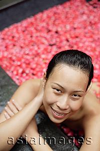 Asia Images Group - Woman leaning on edge of tub filled with floating rose petals, smiling at camera