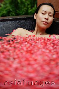 Asia Images Group - Woman in tub filled with floating rose petals, eyes closed