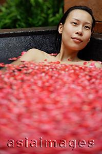 Asia Images Group - Woman in tub filled with floating rose petals, looking away
