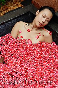 Asia Images Group - Woman relaxing in tub with floating rose petals, eyes closed