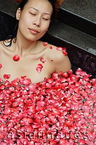 Asia Images Group - Woman with eyes closed, relaxing in tub with floating rose petals
