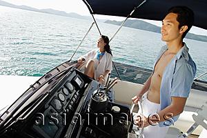 Asia Images Group - Couple on yacht, man steering, woman sitting, looking away
