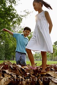 Asia Images Group - Children walking on pile of leaves in park