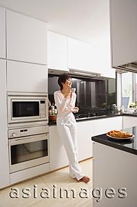 Asia Images Group - Young woman standing in kitchen, having coffee
