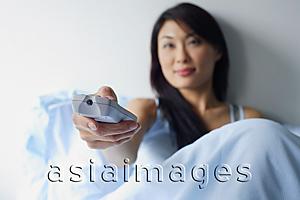Asia Images Group - Woman sitting up in bed, holding TV remote control