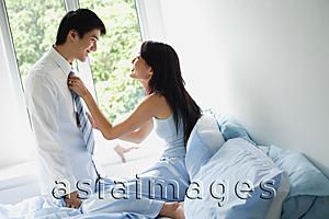 Asia Images Group - Couple in bedroom, woman sitting on bed, adjusting man's tie