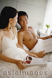 Asia Images Group - Couple sitting up in bed, holding book and magazine