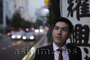 Asia Images Group - Young man standing by busy road, looking up.