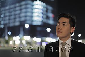 Asia Images Group - Man wearing a suit looking off, lit buildings in background.