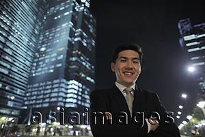 Asia Images Group - Man wearing a suit standing in front of lit buildings at night
