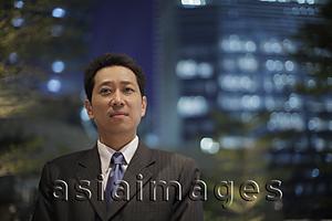 Asia Images Group - Mature man wearing a suit in front of lit buildings at night
