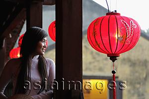 Asia Images Group - Young woman wearing traditional Vietnamese dress looking out from bridge with red lanterns.