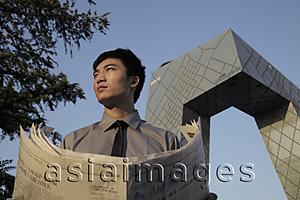 Asia Images Group - Young man holding a newspaper in front of the CCTV Building, Beijing, China