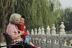 Asia Images Group - Grandmother hugging and kissing grandson in a park