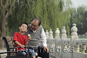 Asia Images Group - Grandfather and grandson in a park eating ice cream