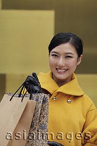 Asia Images Group - Young woman in yellow coat holding shopping bags
