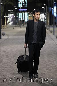 Asia Images Group - Young man walking down a street pulling a suitcase