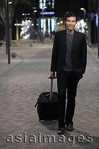 Asia Images Group - Young man walking down street pulling a suitcase