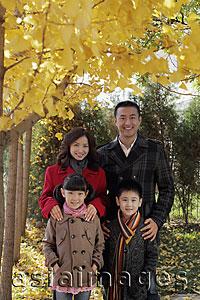 Asia Images Group - Family of four wearing coats standing under a tree with yellow leaves